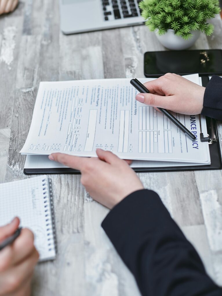 Close-up of hands analyzing insurance policy paperwork with pen on table. SBA Loan Application Step by Step Process